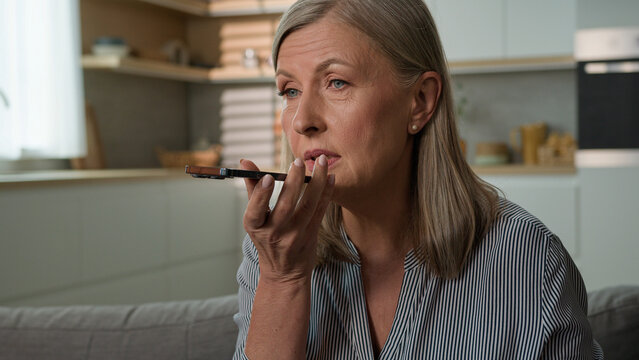 Close-up elderly mature Caucasian woman female grandmother talking on phone using speakerphone at home command internet assistance recording voice message on smartphone mobile ai technology concept