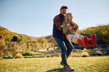 Fototapeta premium Playful man spinning his daughter in nature.
