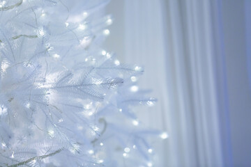 A close-up of a white Christmas tree with soft glowing lights wrapped around delicate branches,...