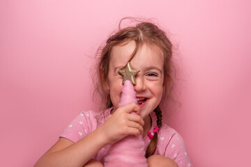 Close up portrait of cheerful young girl with braided hair holding golden star decoration against...