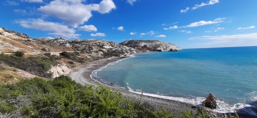 A stunning coastline with turquoise waters, a pebble beach, and rugged hills under a vibrant blue sky. Perfect for travel and nature enthusiasts.