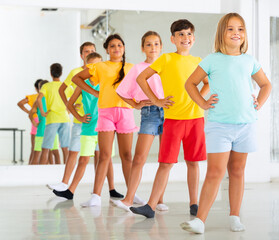 Cheerful preteen girls and boys lined up one after another practicing moves of folk dance during...
