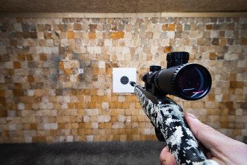 Shooting from a 22 LR rifle with a silencer and optical sight at a paper target in a shooting range.