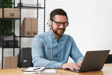 Fototapeta premium Interpreter in headphones having video chat via laptop at wooden table indoors