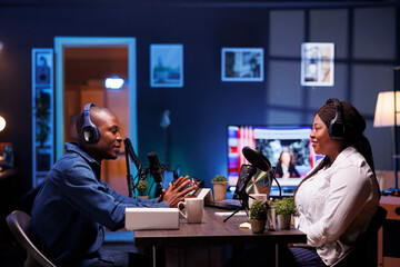 A man and a woman vloggers record a live podcast in a studio using sound production equipment....