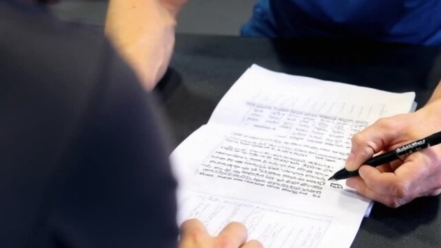 Over-the-shoulder shot of fitness instructor writing a workout plan for a client with blurred gym ambiance in the background.
