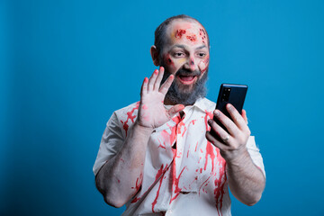 Portrait of actor dressed as horror movie zombie with gore makeup talking in videocall during break...