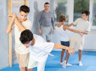 Willing junior attendee of self-defense classes practicing arm twist on a standing boy in sports...