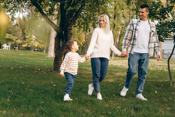 Portrait of smiling family with cute little son waling together outdoors in the park, relaxing