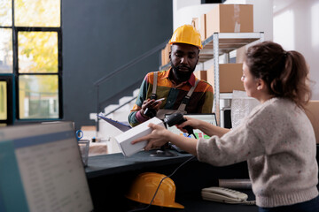 Storehouse manager scanning white box at counter desk, discussing shipping details with aftican...