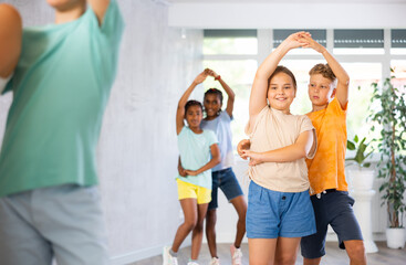 Group of positive juvenile boys and girls doing Tango poses in training room during workout session