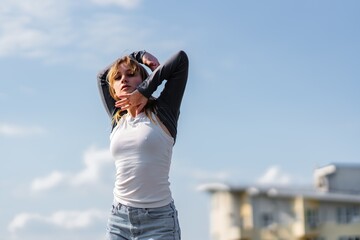 Young woman posing outdoors under a clear blue sky in casual attire