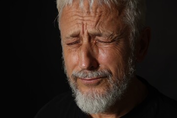 Fototapeta premium Sad senior man crying on black background, closeup