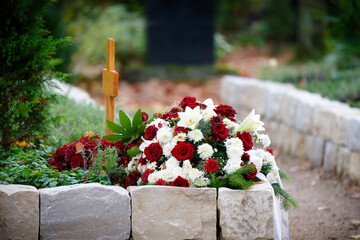 Funeral flowers of red roses and white dahlias and lilies with white ribbon on an urn grave in a modern funeral garden at a burial