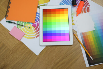 Designer's workplace with tablet, palettes and stationery on wooden table, flat lay