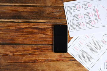 Developing UI design. Sketches of website wireframes and smartphone on wooden table, top view....