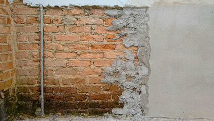 section of old masonry wall undergoing renovation with exposed solid brick section with vertical hydraulic installation pipe and a section with newly installed cement plaster