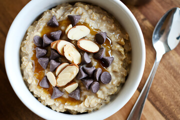 Fototapeta premium Warm oatmeal topped with chocolate chips and almonds served in a bowl for breakfast