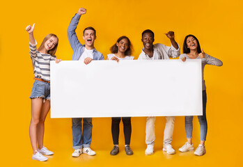 Happy smiling group of multiracial students standing together and displaying white blank placard,...