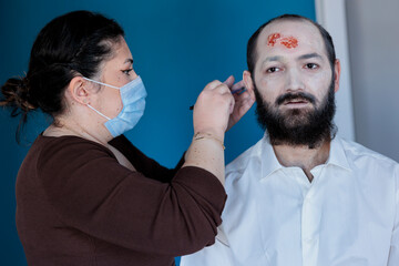 Woman applying foundation on actor face in makeup department, preparing for zombie horror movie...