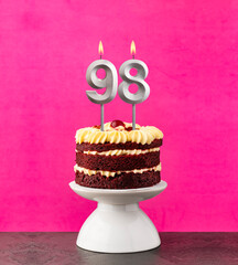 Birthday cake with number 98 candle - Red velvet on a fuchsia background.