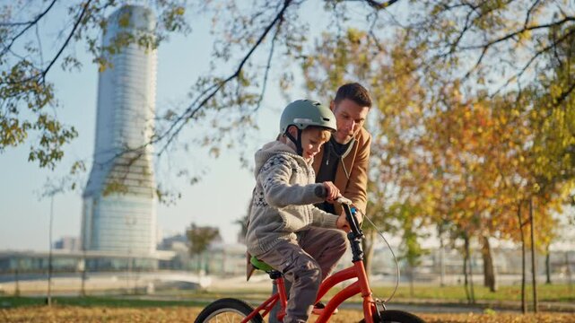 Slow-motion shot of a loving dad teaches his little on to ride bike for the first time in park at sunny day