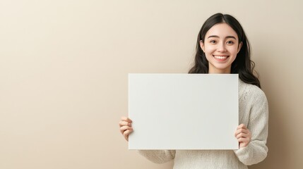 Fototapeta premium Smiling Young Woman Holding a Blank White Sign Against a Beige Background A Perfect Template for Your Message or Advertisement