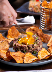 close up of fork mixing and preparing hackepeter meat tartare with raw egg yolk and sweet potato chips