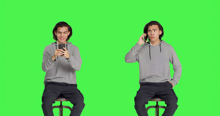 Asian adult texting and answering call on greenscreen background, sending messages on social media using smartphone app. Young man sitting on chair, calling friends and messaging.