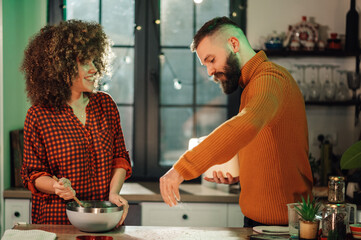 Couple baking together, adding ingredients into bowl in modern kitchen