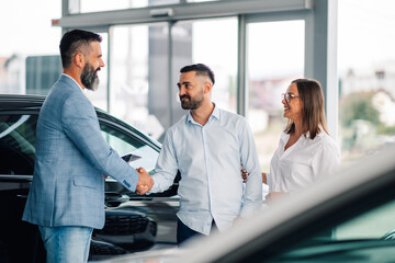 Car dealership handshake marks successful transaction closure.