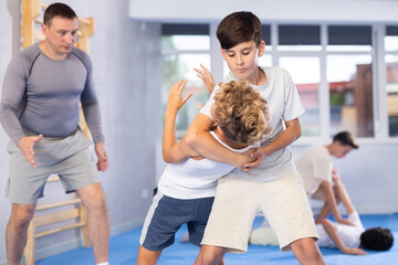 Determined teenage boys practicing inverted facelock self-defense technique in training bout under guidance of experienced instructor at gym..