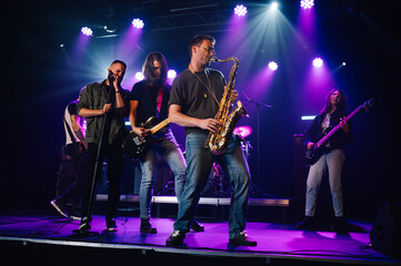 Music band playing live on stage during a concert with purple lights