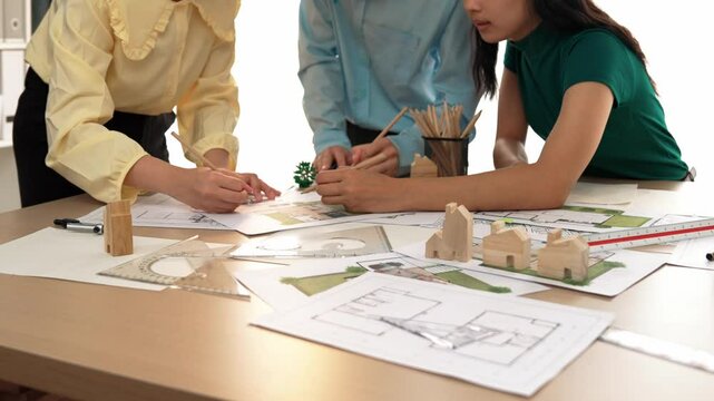Smart architect and safety engineer discussion about building blueprint on table with architectural document, measurement tools and wooden block scatter around at modern office. Closeup. Delineation.
