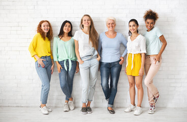 Obraz premium Diverse Ladies Of Different Age Posing Standing Over White Brick Wall Smiling To Camera. Full Length