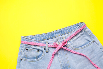 Jeans and measuring tape on yellow background, top view
