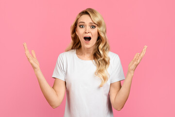 A woman with long blonde hair is standing against a pink background. She has an astonished...