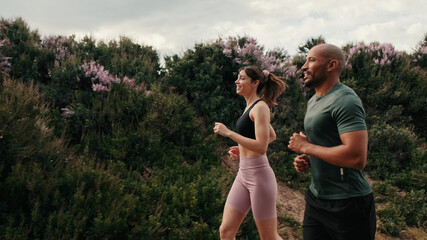 Side view of jogging multiethnic woman and man enjoy their outdoors workout in summer. Team sports. Couple goals and motivation. Happy fit people are cheerfully doing sports