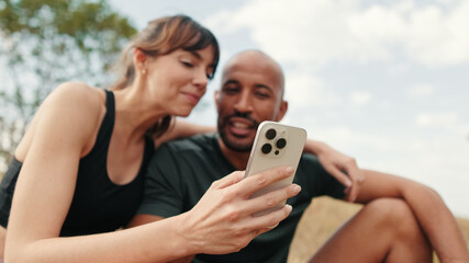 Close-up of athletic couple in love relaxing and using smartphone, focus on the mobilephone