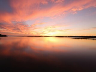 Naklejka premium Vibrant sunrise over a calm lake, illuminating the sky with warm orange and pink hues, orange, reflection