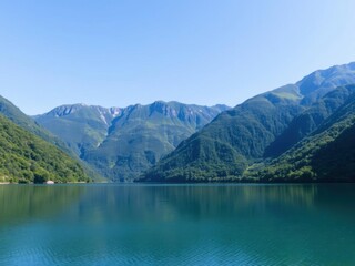 Photo of a serene lake surrounded by lush green mountains under a clear blue sky, vacation, outdoor