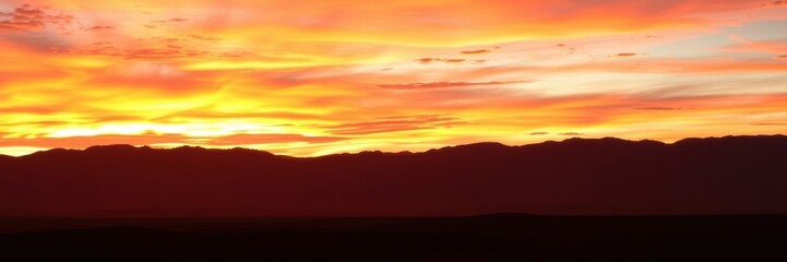Fototapeta premium Vibrant desert sunset with silhouetted mountains in the background, vibrant, dusk