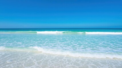Fototapeta premium Soft blue ocean wave gently rolling onto a beautiful sandy beach on a sunny day, summer, relaxation