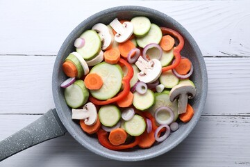 Frying pan with mix of fresh vegetables and mushrooms on white wooden table, top view