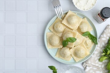 Delicious ravioli with cheese and basil served on white tiled table, flat lay. Space for text