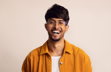 Obraz premium Closeup portrait of happy bearded arabic guy wearing glasses laughing at camera over grey studio background, copy space. Handsome middle-eastern young man in casual showing positive emotions