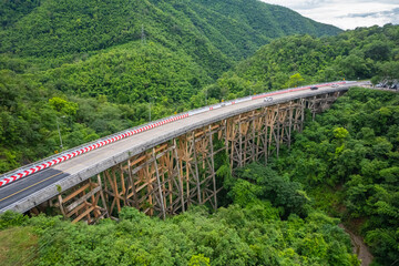 An aerial view of Phor Khun Pha Muang Bridge, or Huai Tong Bridge in Phetchabun, showcases its majestic span through a high mountain pass, connecting northern and northeastern Thailand