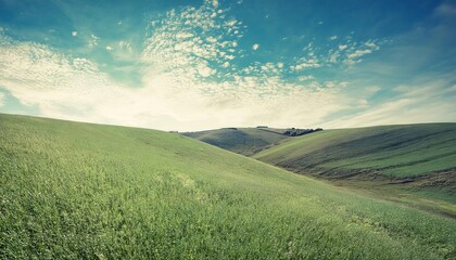 Fototapeta premium Scenic countryside view with green fields, rolling hills, and a bright sky during sunrise or sunset