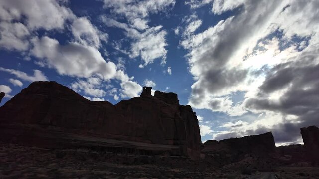View from vehicle driving by the Tower of Babel in Arches National Park tracking the red rock cliff while moving by.
