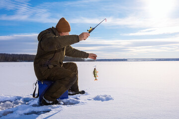 Man ice fishing on frozen lake at sunny winter day. Ice fishing.